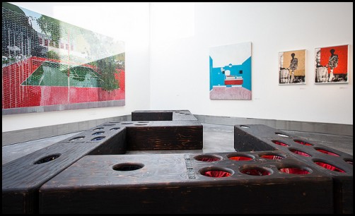 Foreground: Nari Ward 'Domino Men', 2011, 28 dominoes, burnt wood, tires, used clothes, 208 x 61 x 48cm.