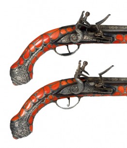 Pair of Algerian coral-inlaid flintlock holster pistols; barrels octagonal at the breech, inlaid with engraved silver; stocks mostly covered with shaped red corals retained by engraved silver cage-work.  Pistols fitted with silver furniture. 18th century