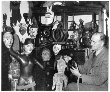 James Hooper (1897–1971) in the Totems Museum, Arundel, c.1958, holding a South American Shuar (Jivaro) shrunken head and surrounded by mostly African artefacts.